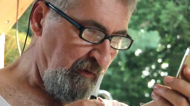 Senior skäggig man trimmar sin ögonbryn och hår med liten sax — Stockvideo