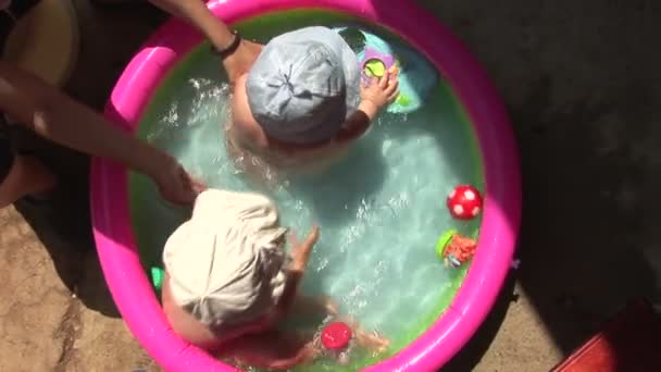 Ein kleines Mädchen und ein Junge spielen im Pool. Spritzer und Schlag ins Wasser — Stockvideo