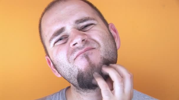 Чоловік на жовтому тлі дряпає бороду — стокове відео