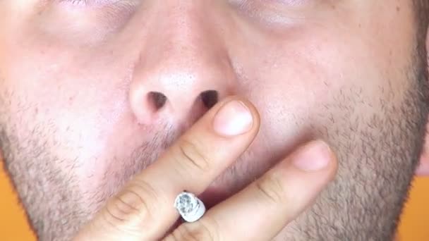 Мужчина смотрит в камеру и курит — стоковое видео