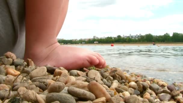 Jonge jongen zittend op een bank van de rivier spelen met stenen — Stockvideo