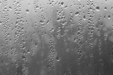 Gri arka plandaki pencere camına yağmur damlaları. Yağmur damlalarının doğal deseni. Yaratıcılık için doku. Camın yüzeyinde su var..