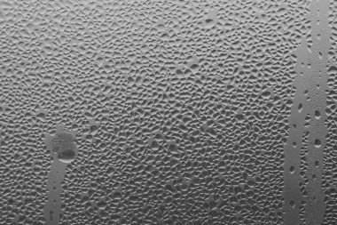 Gri arka plandaki pencere camına yağmur damlaları. Yağmur damlalarının doğal deseni. Yaratıcılık için doku. Camın yüzeyinde su var..