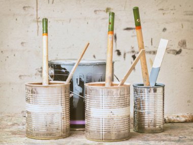 Lekeli bir duvarın önünde kullanılmış boya kovaları ve fırçalar.