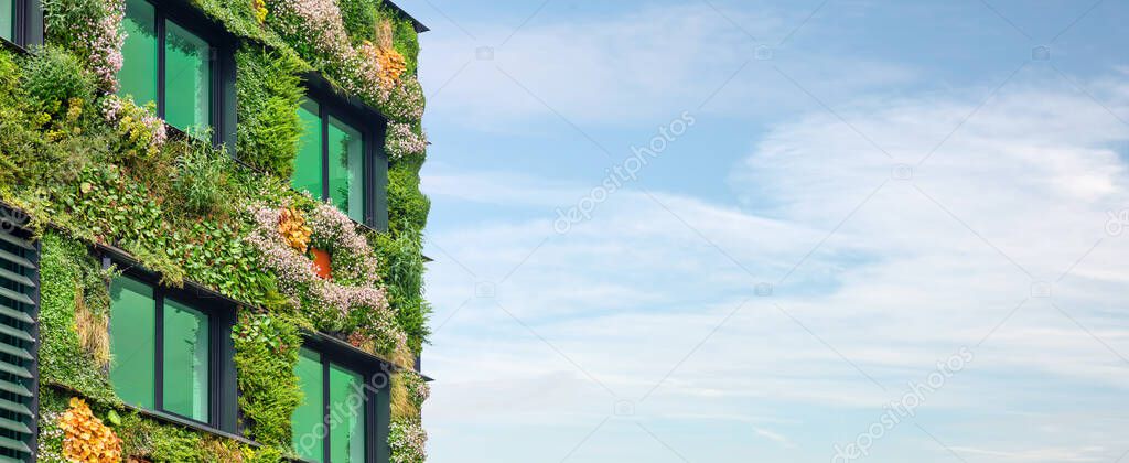 Exterior of a green sustainable building covered with blooming vertical hanging plants in front of a blue sky