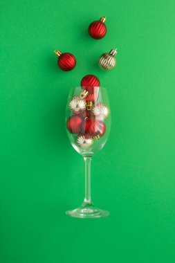 Kırmızı ve yeşil arka planda altın topları olan şarap kadehi. Yakın plan. Konum dikey.