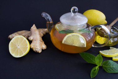 Siyah zemin üzerinde limon, zencefil ve bal olan cam çaydanlığa yakın plan.