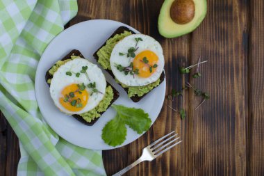 Kahvaltıda çavdar ekmeği, avokado püresi, sahanda yumurta ve ahşap arka planda mikroyeşil ile avokado tostlarının üst görüntüsü. Boşluğu kopyala.