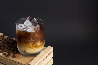 Siyah arka plandaki tahta kutunun üzerindeki içme bardağında soğuk demlenmiş kahve. Boşluğu kopyala.