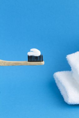 Bambu diş fırçasına yakın plan beyaz macun ve mavi arka planda beyaz havlular. Konum dikey.