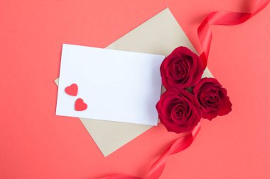 Metin için boş beyaz kağıdın üst görünümü, kırmızı yüzeyde kırmızı güller ve kalpler