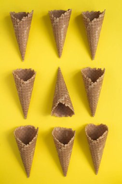 Sarı arka planda kremalı dondurma külahları yatıyordu. Yakın plan. Konum dikey.