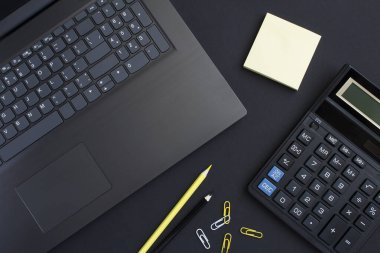 Bilgisayarlı, hesap makineli ve siyah arka planlı ofis masasının üst görüntüsü. Yakın plan. Çalışma masasının düz uzantısı.