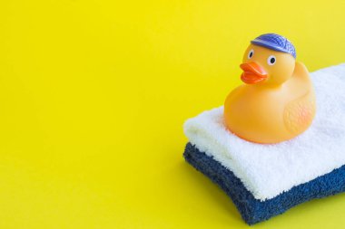 Sarı arka planda havluyla yıkanmak için sarı oyuncak ördek yavrusuna yakın plan. Boşluğu kopyala.