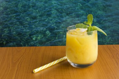 Denizin arka planına karşı ahşap masadaki içme bardağında buzlu portakal suyu. Boşluğu kopyala.