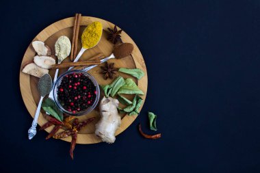 Top view of various spices on thw wooden cutting board on the  black background. Copy space.