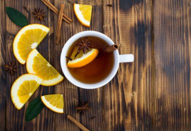 Top view of tea with orange, cinnamon and anise in the white cup on the wooden  background. Copy space.