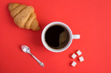 Kırmızı arka planda kruvasan ve kahve fincanı var. Uzayı kopyala Yakın plan..