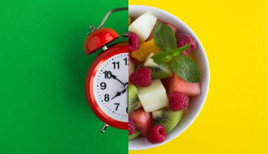 Kırmızı alarm saati kolajı ve renkli arka planda meyveli sağlıklı salata. Üst Manzara. Boşluğu kopyala.