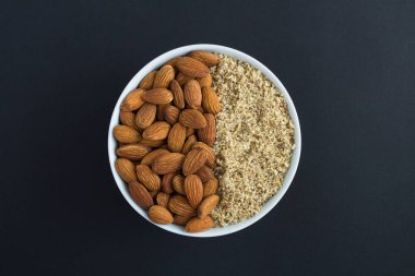 Siyah arka plandaki beyaz kasede kurutulmuş ve doğranmış badem. Üst Manzara. Yakın çekim..