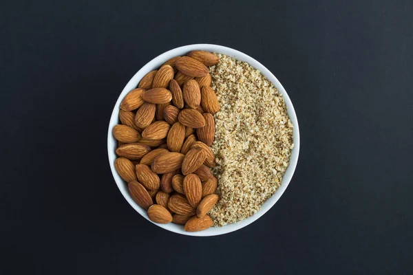 Siyah arka plandaki beyaz kasede kurutulmuş ve doğranmış badem. Üst Manzara. Yakın çekim..