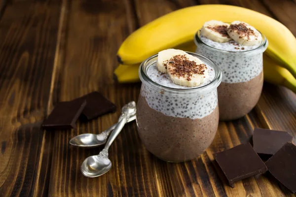 Chocolate pudding with chia seed and banana in the glass jars on the wooden background. Closeup.