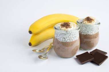 Beyaz arka planda cam kavanozların içinde chia tohumu ve muz olan çikolatalı puding. Boşluğu kopyala.