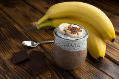 Ahşap arka planda cam kavanozda chia tohumu ve muz olan çikolatalı puding. Yakın çekim..