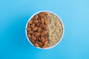 Mavi arka plandaki beyaz kasede kurutulmuş badem. Üst Manzara. Yakın çekim..