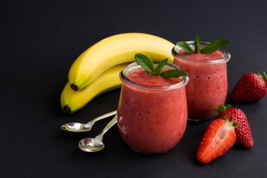 Siyah arka plandaki cam kavanozda çilekli ve muzlu meyve püresi. Uzayı kopyala Yakın plan..