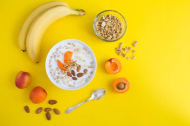 Sütlü granola kahvaltısı, sarı arka plandaki beyaz kasede meyve ve badem. Uzayı kopyala Üst görünüm.