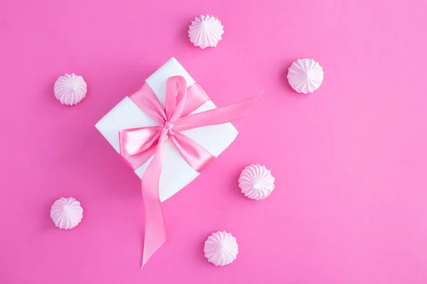 Gift box with tied pink bow and macaroon on the pink background. Closeup. Top view.