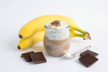 Beyaz arka planda cam kavanozda chia tohumu ve muz olan çikolatalı puding. Yakın çekim..