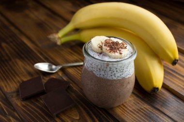 Ahşap arka planda cam kavanozda chia tohumu ve muz olan çikolatalı puding. Yakın çekim..