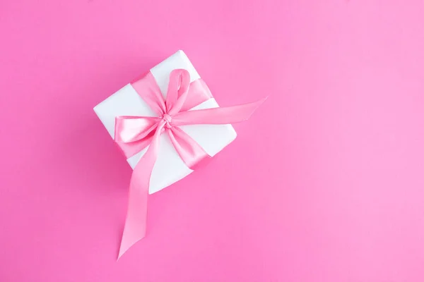 Gift box with tied pink bow on the pink background. Closeup. Top view.