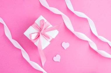 Pembe kurdeleli hediye kutusu, kurdele ve pembe arka planda iki pembe kalp. - Yakın çekim. Üst görünüm.