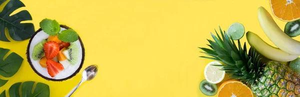 Banner. Tropical fruits and fruit salad in half coconut on the yellow background. Close-up. Copy space.
