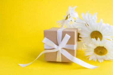 Sarı arka planda bağlı beyaz fiyonklu bir hediye kutusu ve papatya çayı. - Yakın çekim. Boşluğu kopyala.