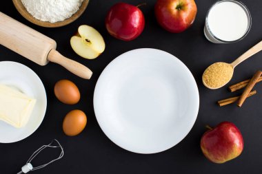 Boş beyaz tabak ve siyah arkaplanda elmalı turta ya da kek yapmak için malzemelerin üst görüntüsü. Boşluğu kopyala.