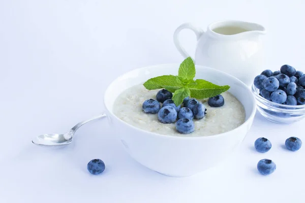 Oatmeal with milk and blueberry in the white bowl on the white background. Healthy breakfast. Copy space.