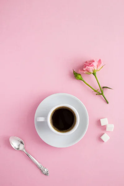 Black coffee in the white cup and pink roses on the pink  background. Top view. Location vertical.