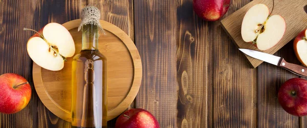 Banner. Top view of apple vinegar cider in the glass bottle and red apples on the wooden  background. Copy space.