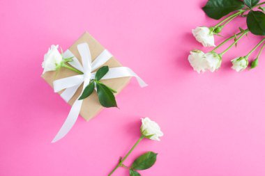 Gift box and white roses on the pink background.Top view. Copy space.