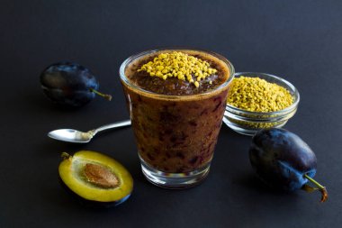 Smoothie with blue plums and  bee pollen on the black background. Close-up.