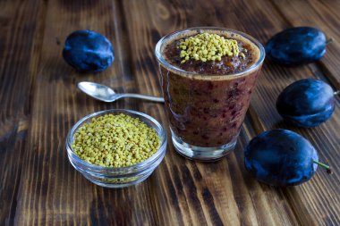 Smoothie with blue plums and  bee pollen on the wooden background. Close-up.
