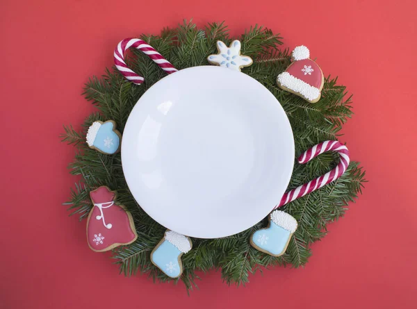 Empty white plate and Christmas composition on the red background. Top view. Copy space.