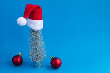 Christmas silver tree with Santa Claus hat on the blue background.Copy space. Close-up.