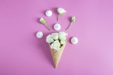 Ice cream cone with white roses and meringue the pink background. Top view. Close-up. Copy space.
