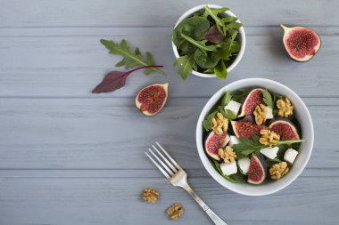 Arugula salatası, feta peyniri, incir ve ceviz gri ahşap arka planda beyaz kasede. Üst Manzara. Boşluğu kopyala.
