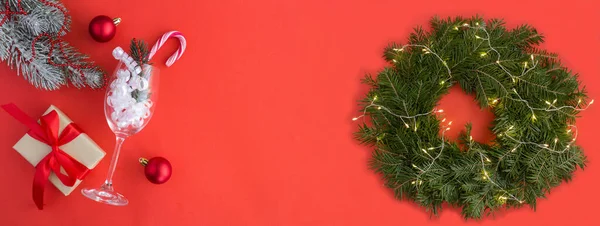 Christmas banner.Christmas wreath, gift box hristmas and champagne glass on the red background. Copy space.